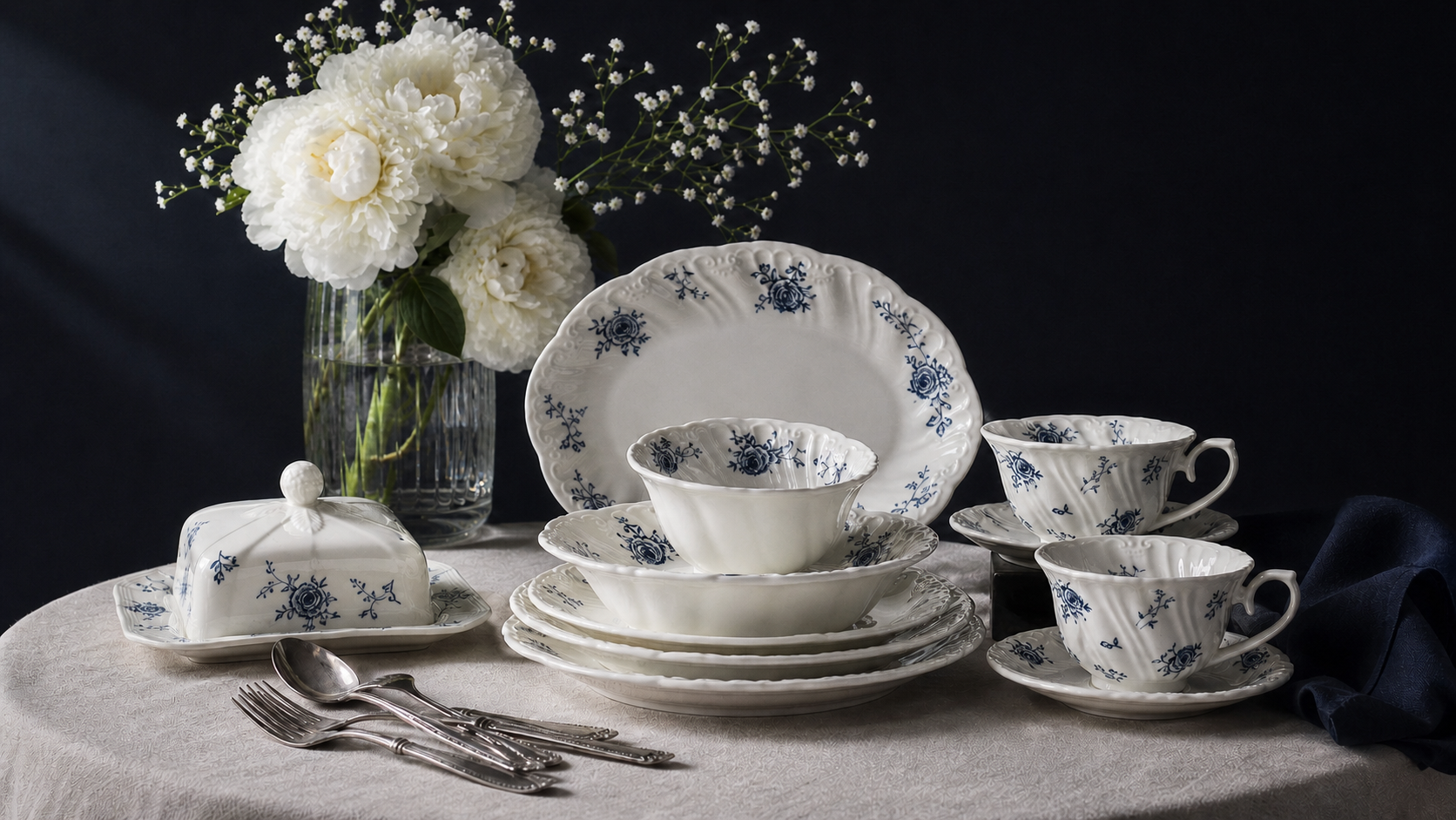 Ivory Lace blue rose dinnerware and serving pieces arranged in a dark still-life table setting