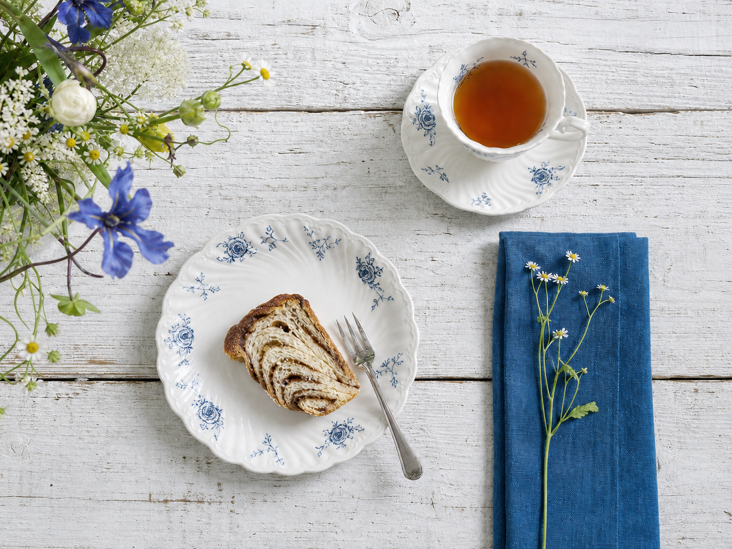 Ivory Lace plate and teacup arranged with pastries and blue linen on a white table