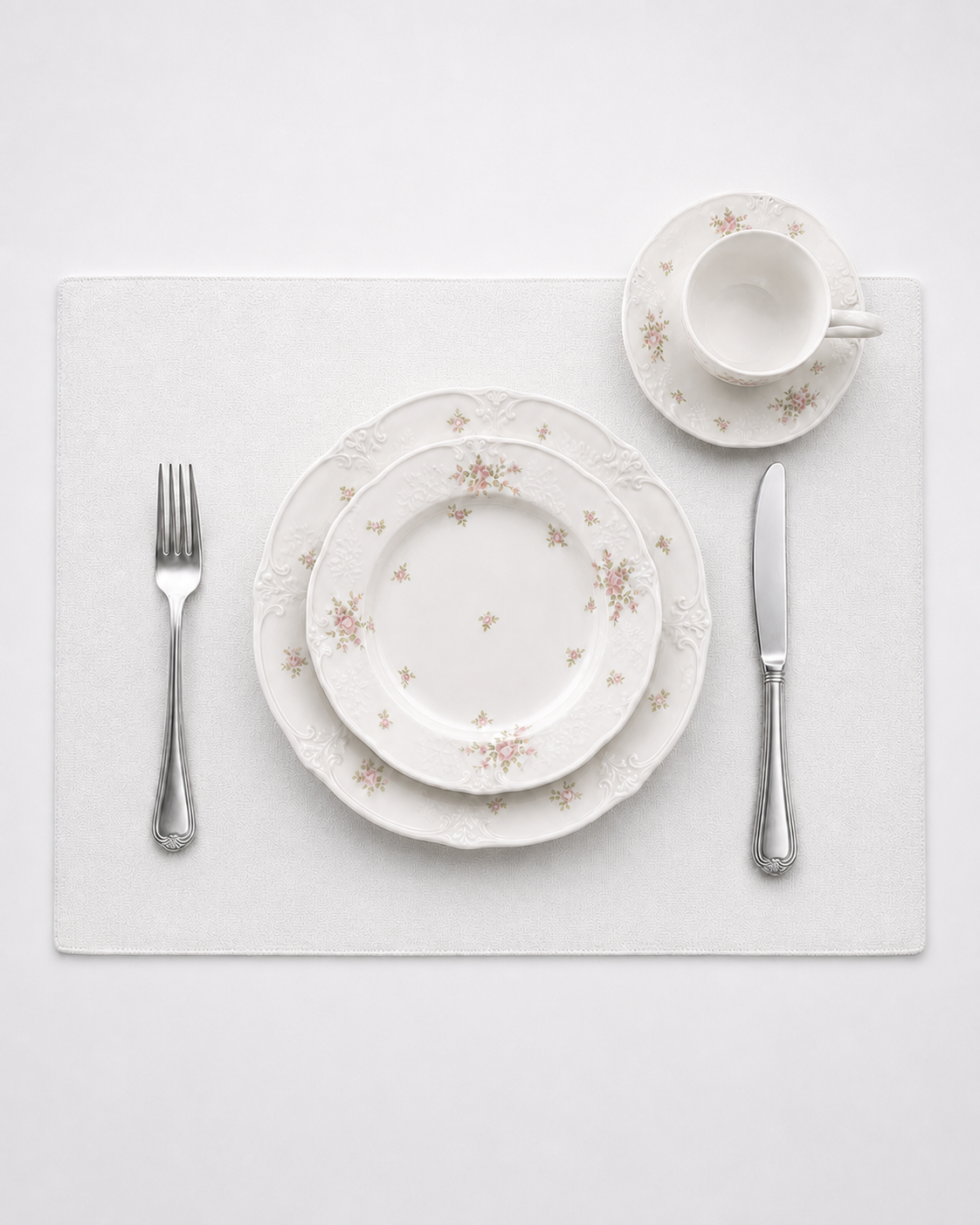 Top-down Meadow Bloom place setting with layered plates, cup and saucer, fork and knife