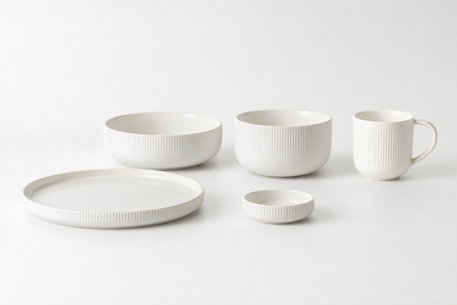 Warm-white ribbed ceramic plate, bowls, mug, and sauce dish arranged as a coordinated collection