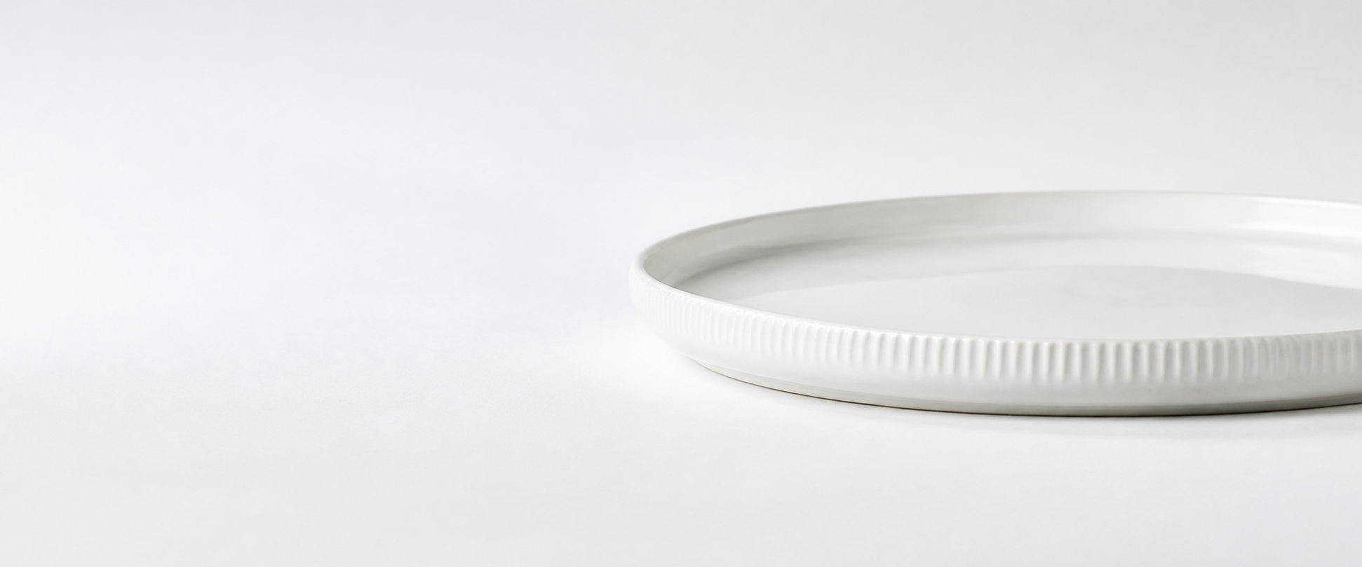 Close view of the low rim and fine vertical relief on a warm-white ceramic dinner plate