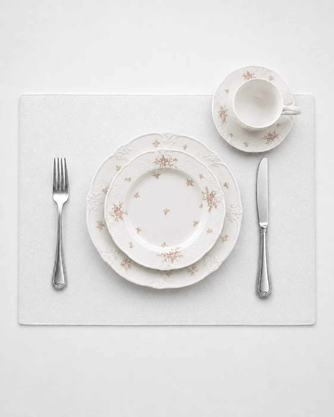 Top-down Blush Posy place setting with layered plates, cup and saucer, fork and knife