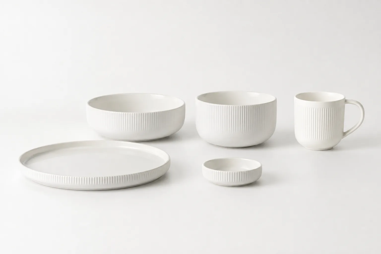 Five coordinated warm-white ceramic forms in a quiet collection display