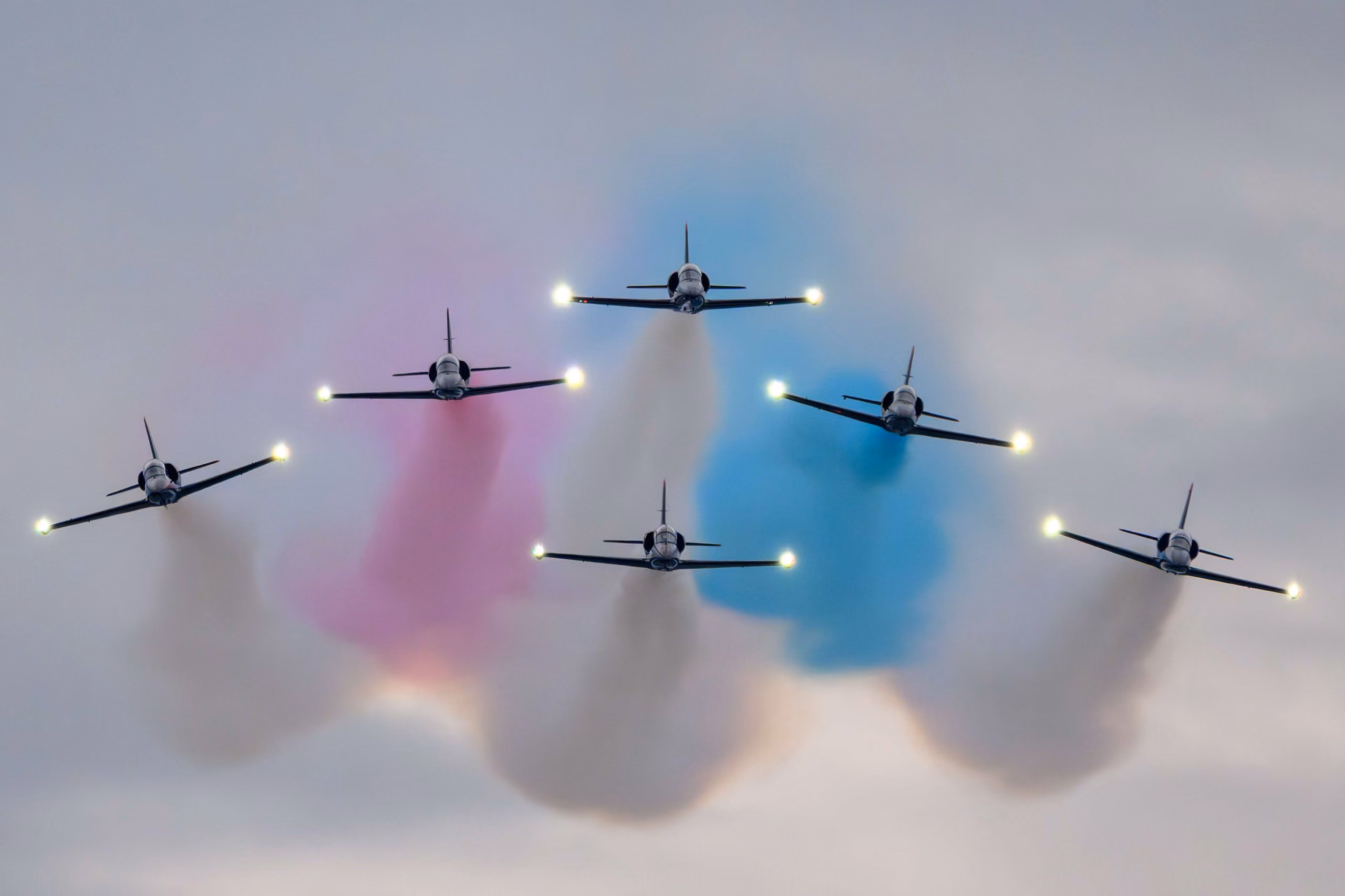 group of planes flying in formation with blue and pink smoke