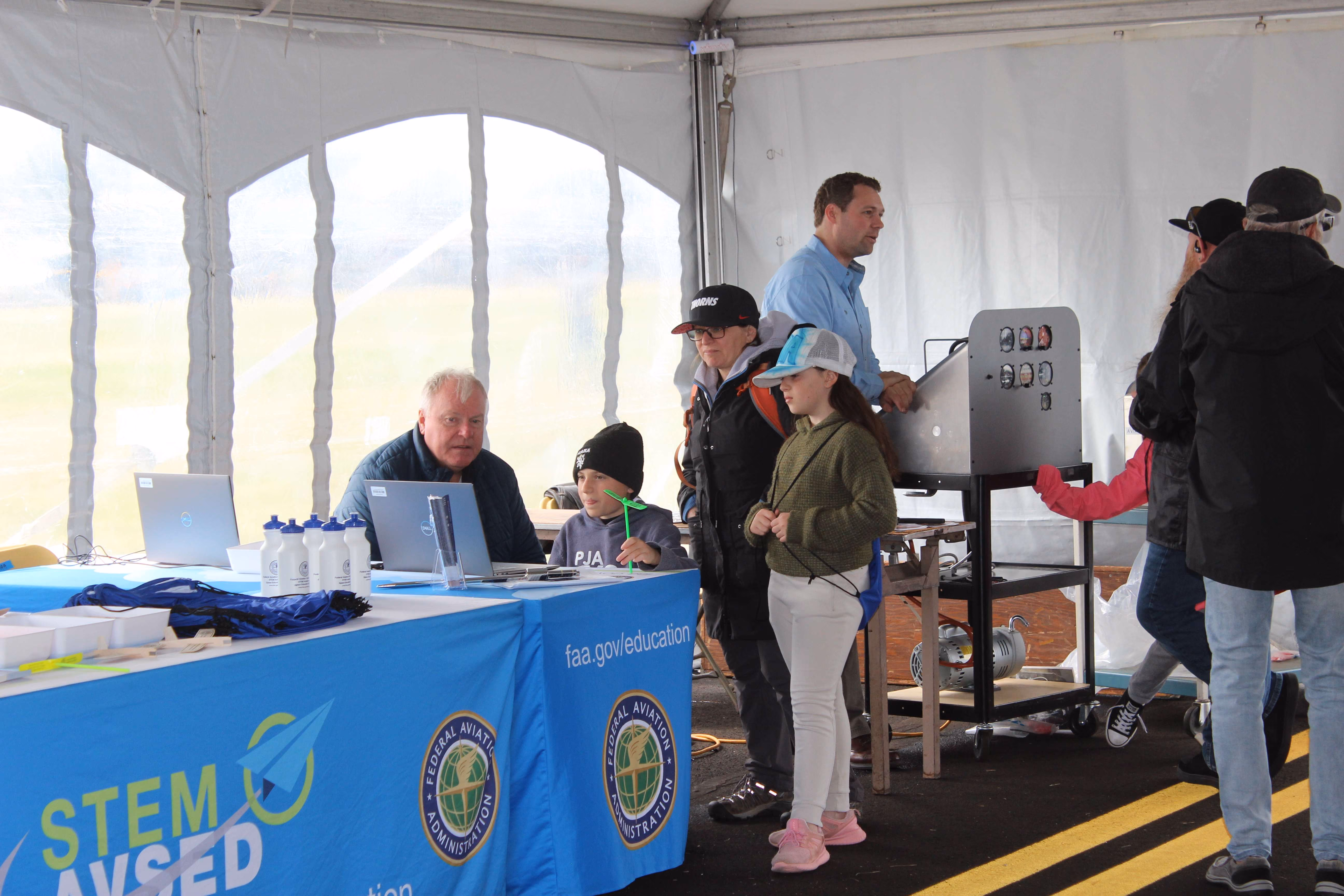 people at an interactive stem display under tent at air show