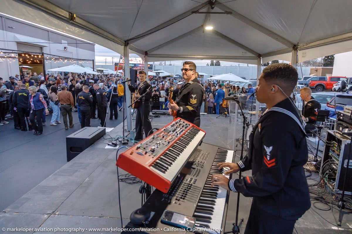 band playing musical instruments under tent with large crowd watching