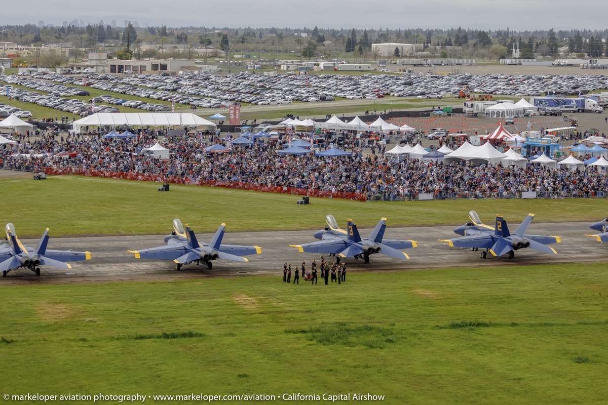 Four large planes lined up with large crowd of people behind it