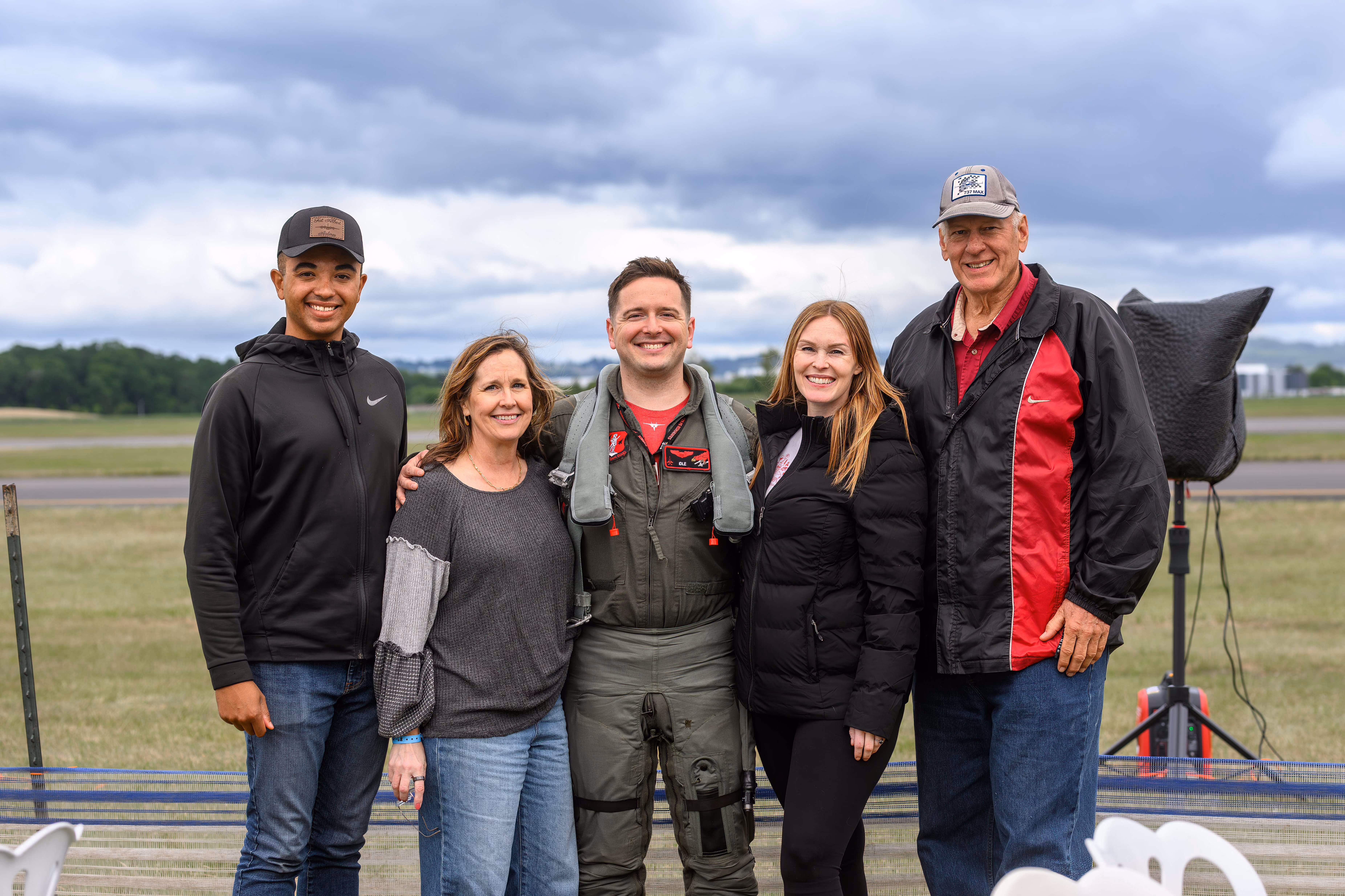 group of smiling people in front of grass field at air show