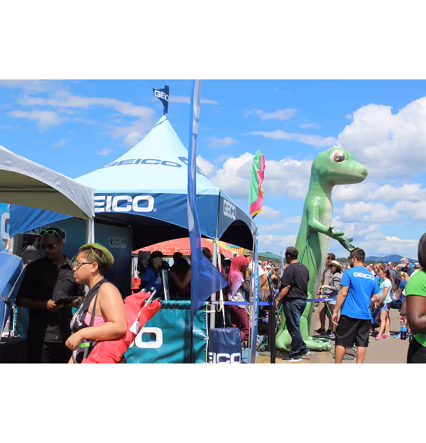 GEICO lizard inflatable in front of marketing tent with people surrounding it