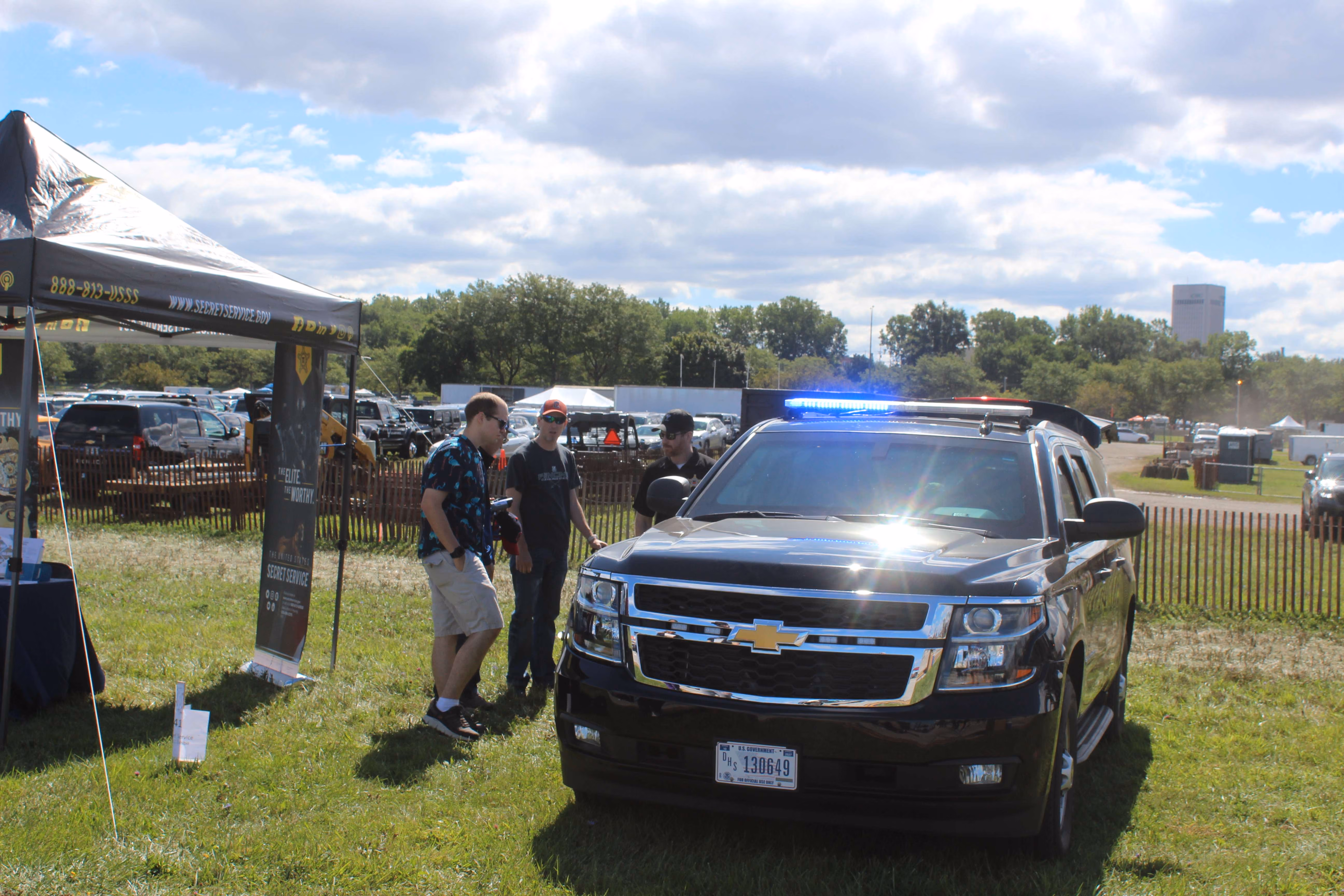 vehicle with blue lights being observed by group of people in grass field at air show