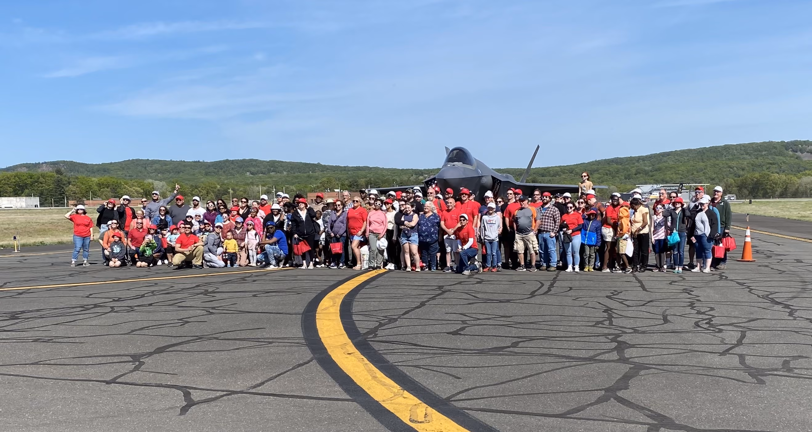 large group of people standing and smiling in front of air plane on tarmac