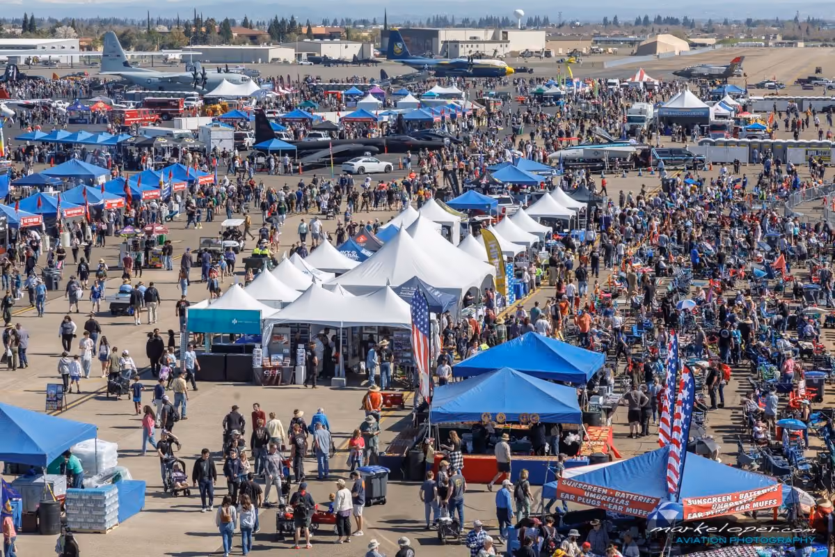 aerial view of air show with large crowd of people surrounding various tents with airplanes in background