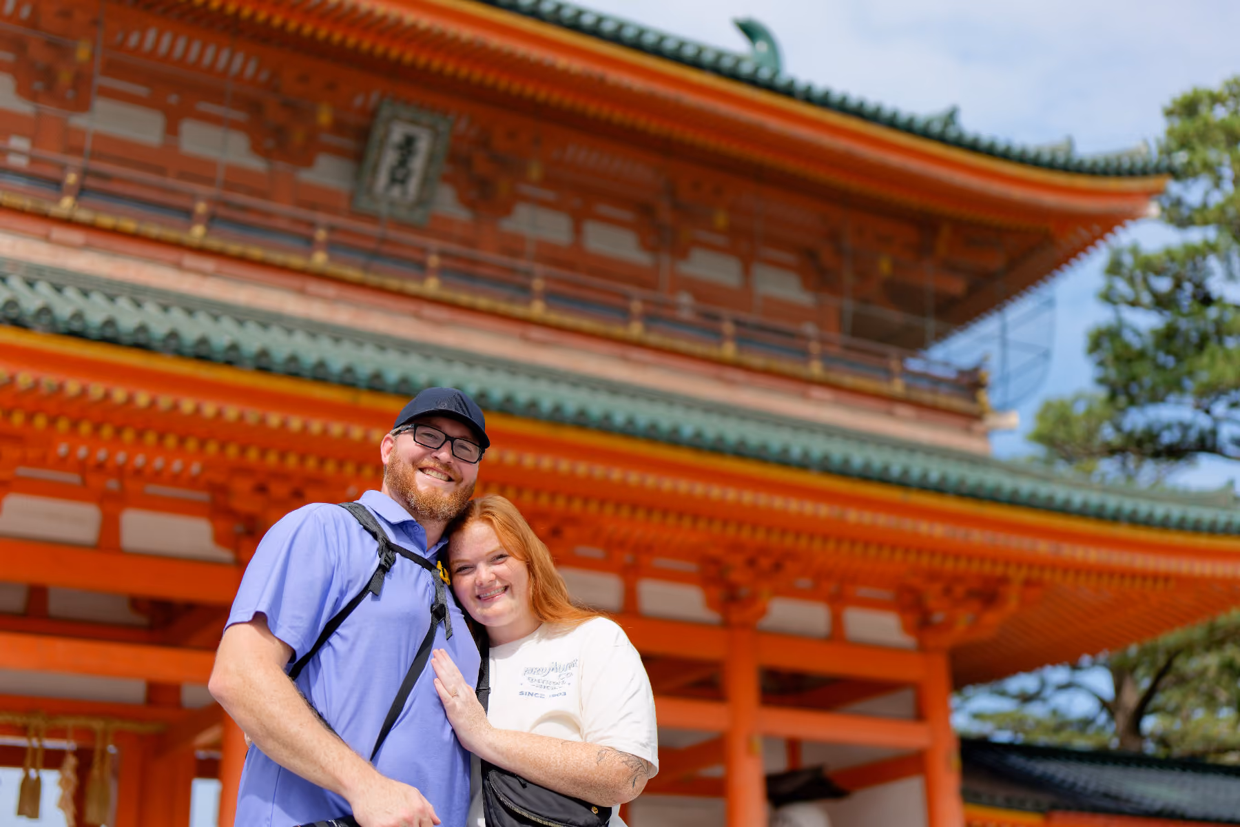 Smiling couple posing in front of an ornate traditional Asian temple with red and green details.