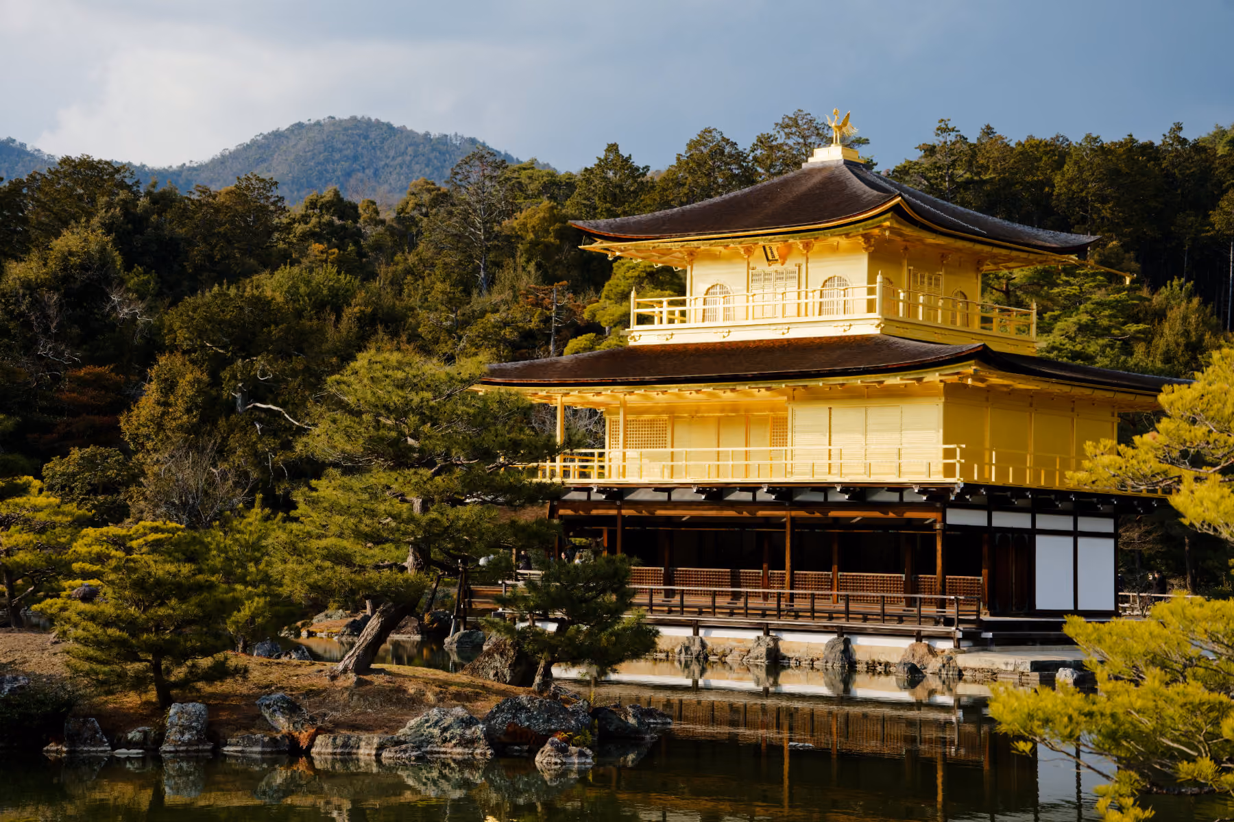 Golden Pavilion temple reflecting in pond surrounded by trees and mountains in Kyoto, Japan.