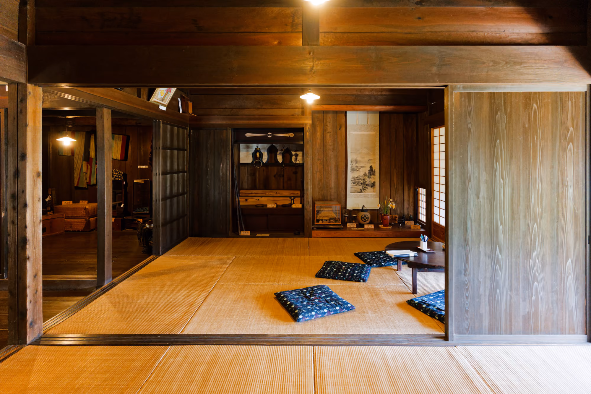 Traditional Japanese room with tatami mats, low wooden table, blue cushions, and wooden walls with decor.