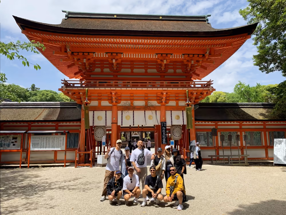 Group of nine people posing in front of a large traditional red Japanese temple gate.