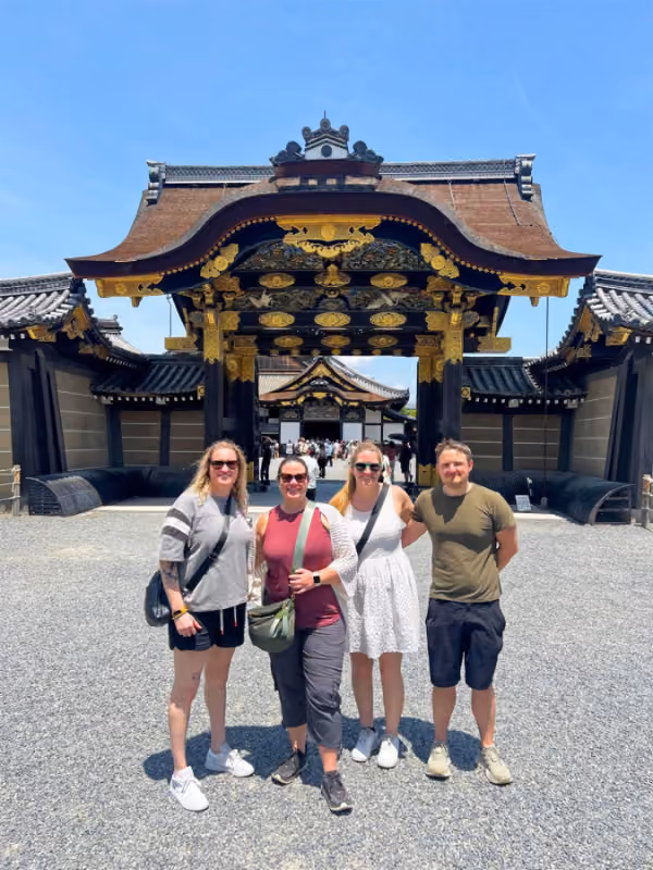 Four people posing in front of an ornate traditional Japanese gate on a sunny day.