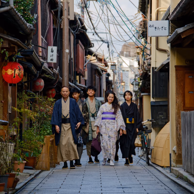 Five people walking down a narrow street in traditional Japanese clothing and kimonos.