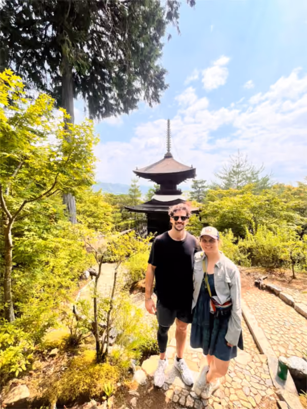 Man and woman standing on stone path in a green garden with a traditional pagoda in the background.
