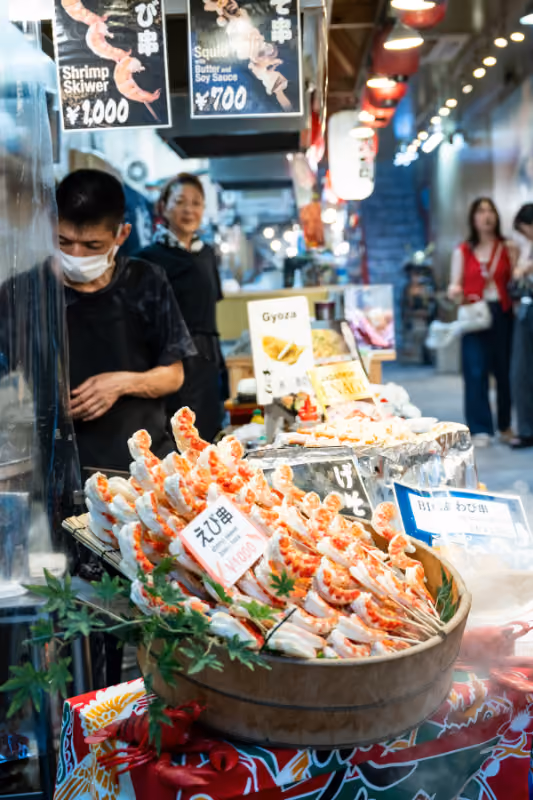 Market stall displaying skewered shrimp with price tags and two people behind the counter.