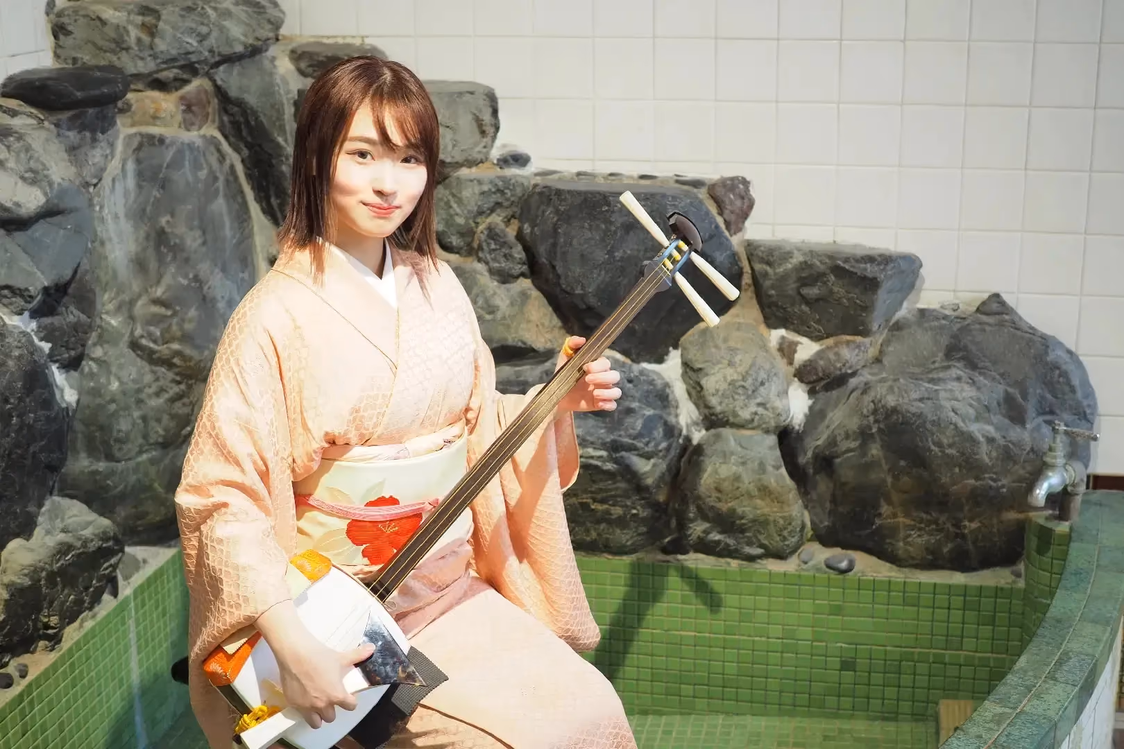 Shamisen player in a peach kimono seated beside the tiled bath at Gen Soundbath Kujo-yu, Kyoto