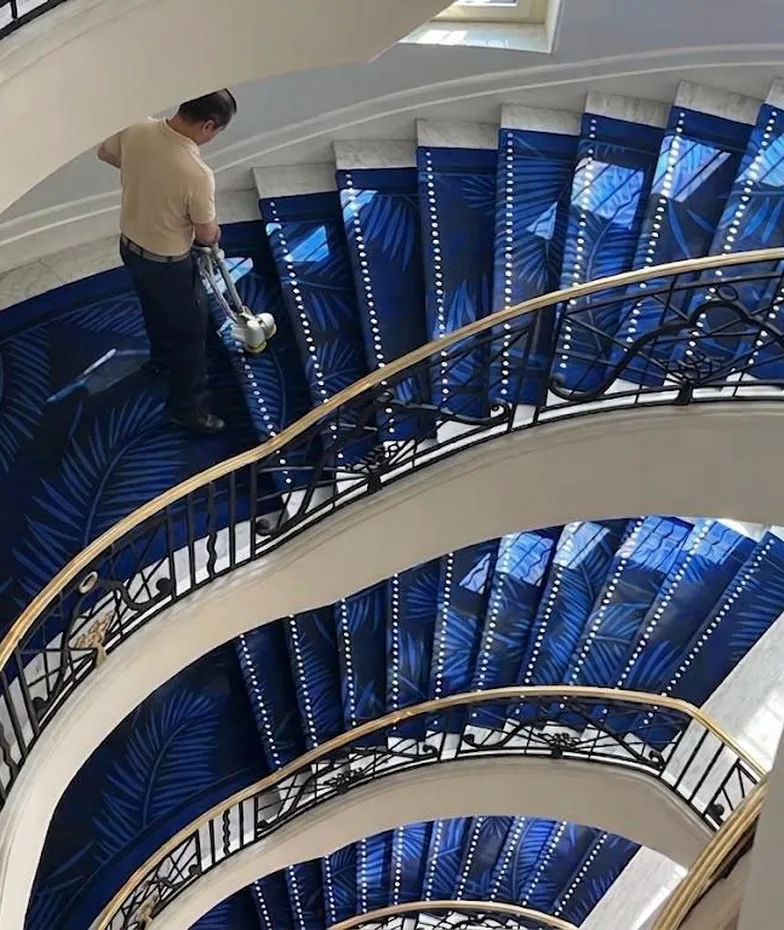 Technicien Mocade nettoyant la moquette bleue d’un escalier en colimaçon