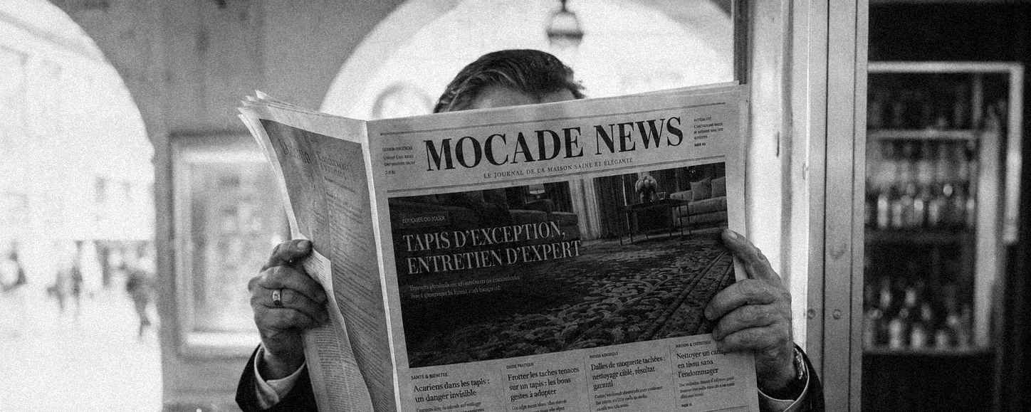Lecteur dépliant un journal Mocade News dans un hall, photographie en noir et blanc