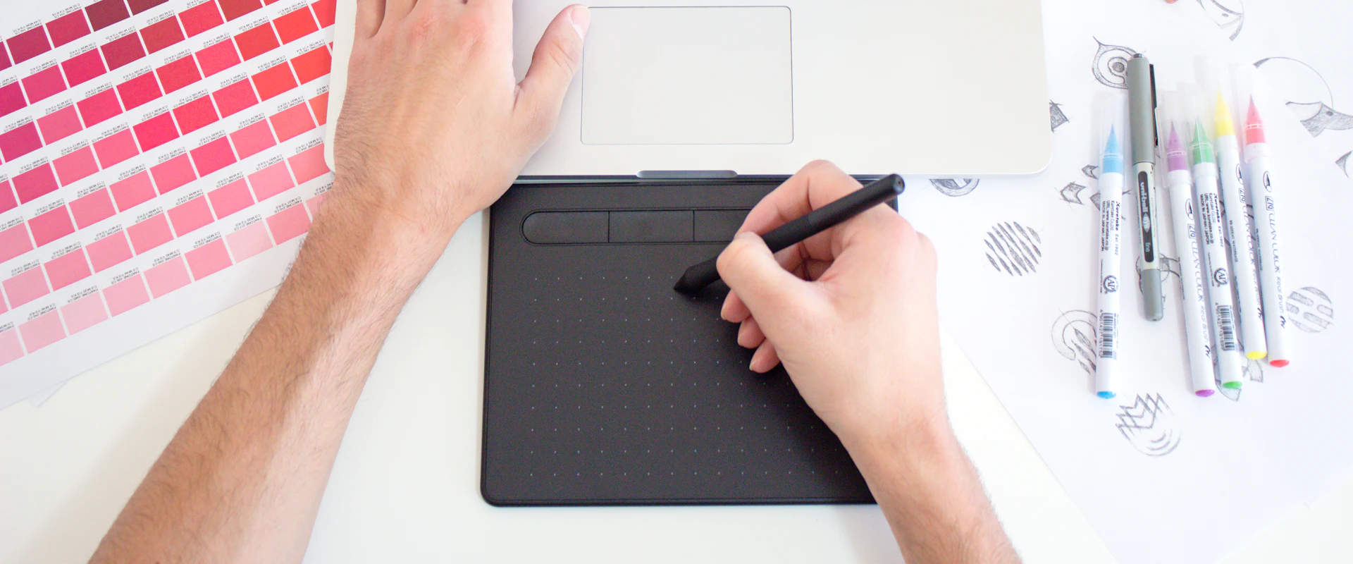 Designer working on a drawing tablet beside color swatches and markers