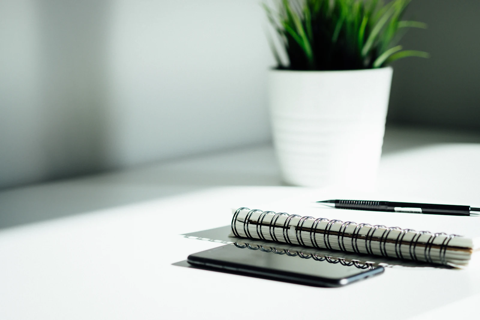Notebook, pen and phone on a white desk