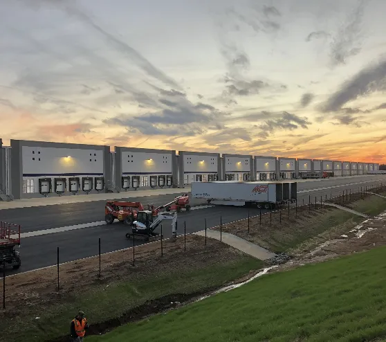 A distribution centre's loading dock frontage at dusk, with a trailer at the bay and site work still under way