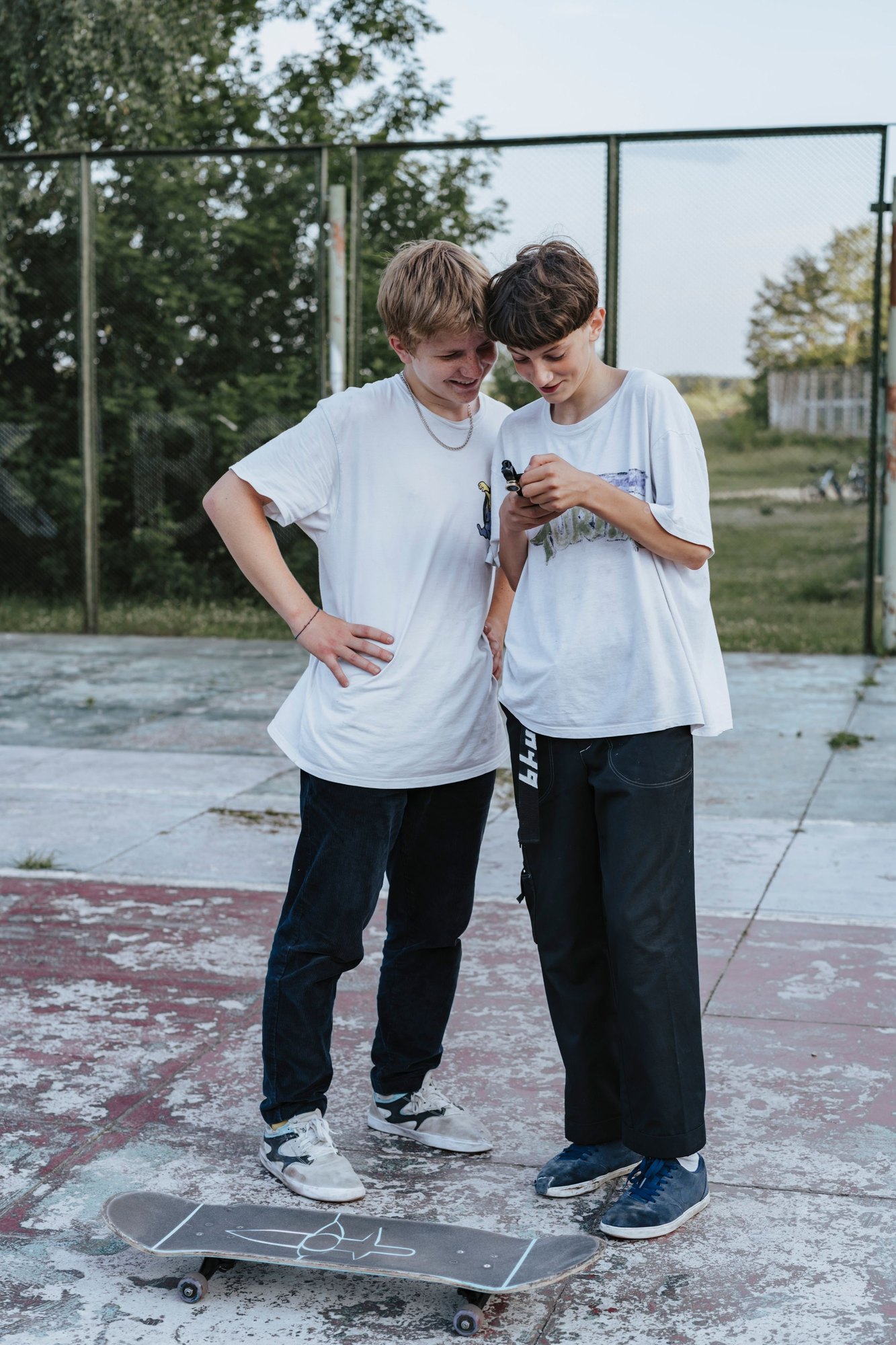 Two teenagers standing together outdoors beside a skateboard