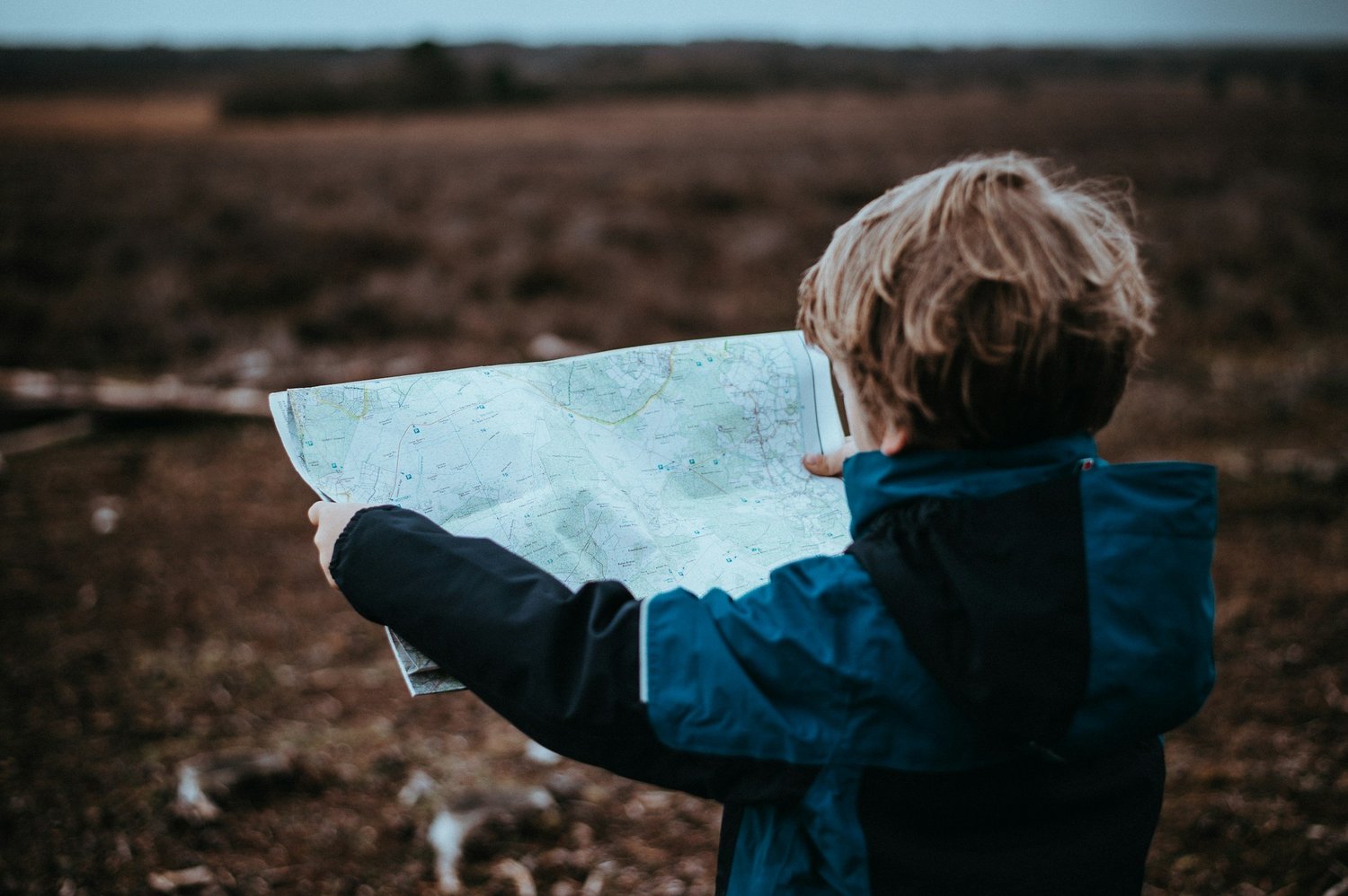 A child in a blue coat holding an open map in a bare field