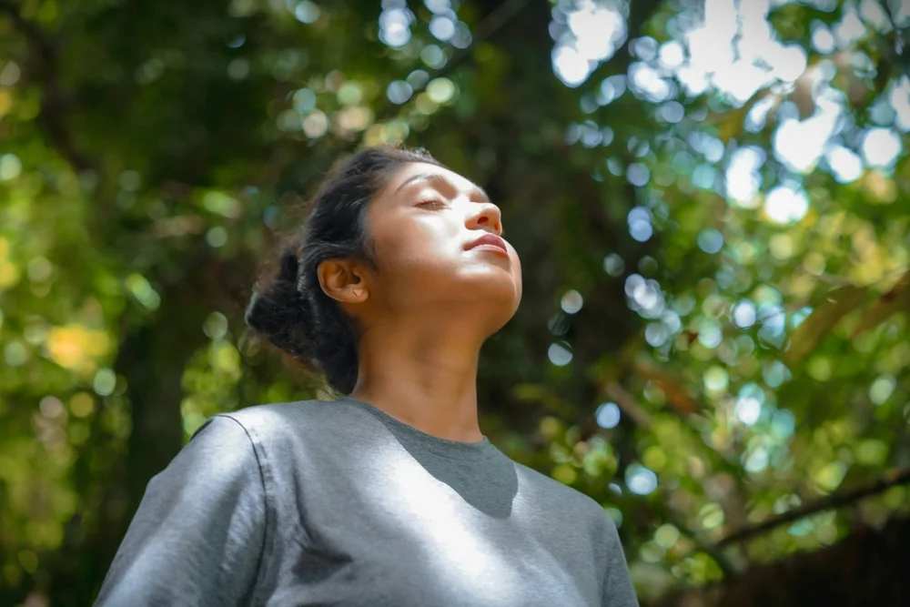 A woman standing outdoors with her face tilted up and eyes closed