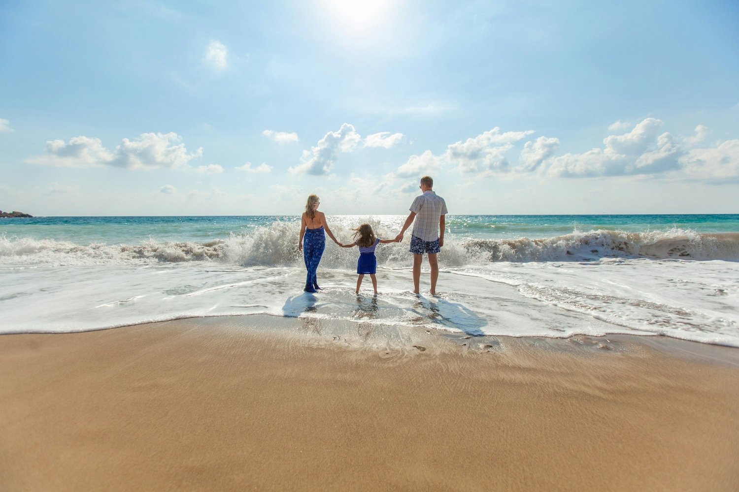 A family of three standing at the edge of the surf, seen from behind