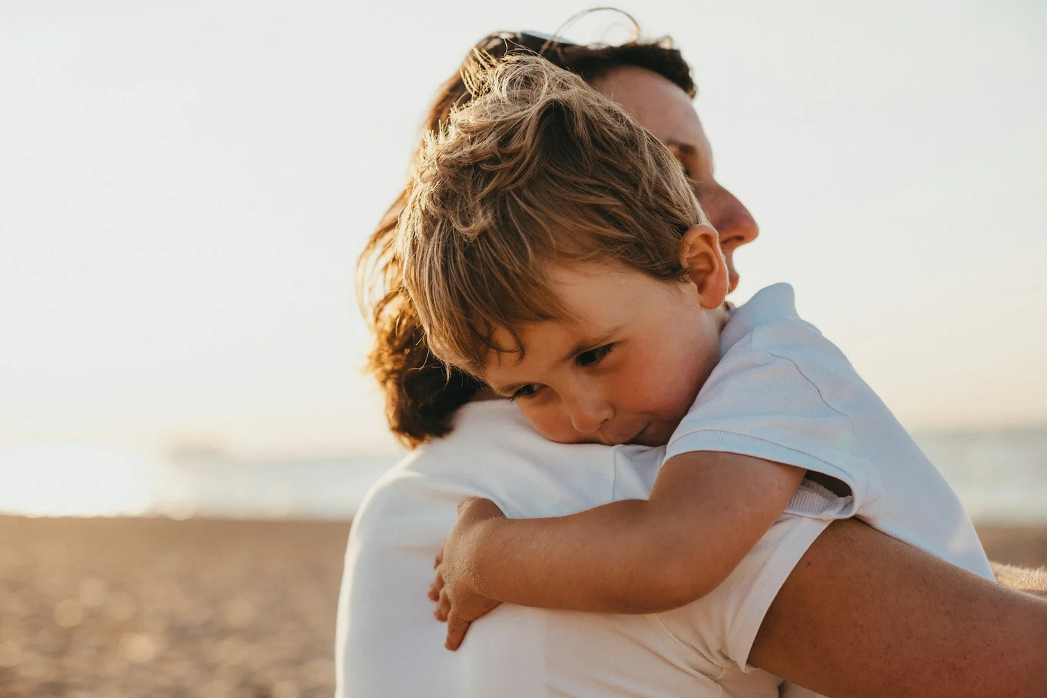 An adult carrying a young child on their shoulder outdoors