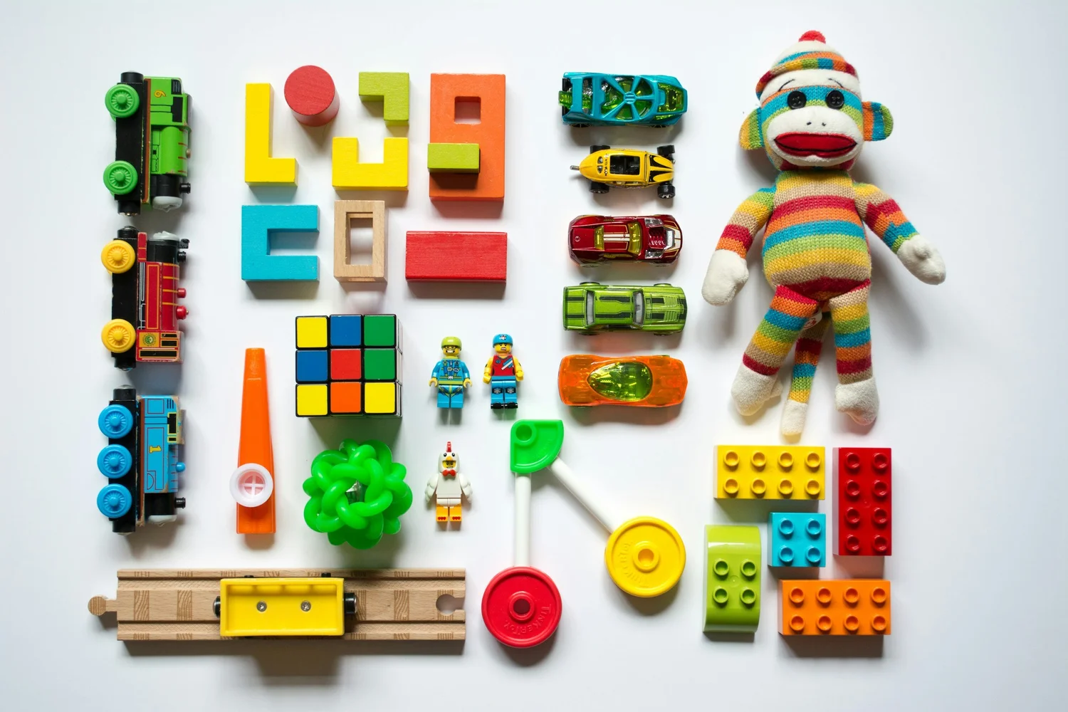 A flat lay of wooden and plastic toys including a sock monkey and building bricks