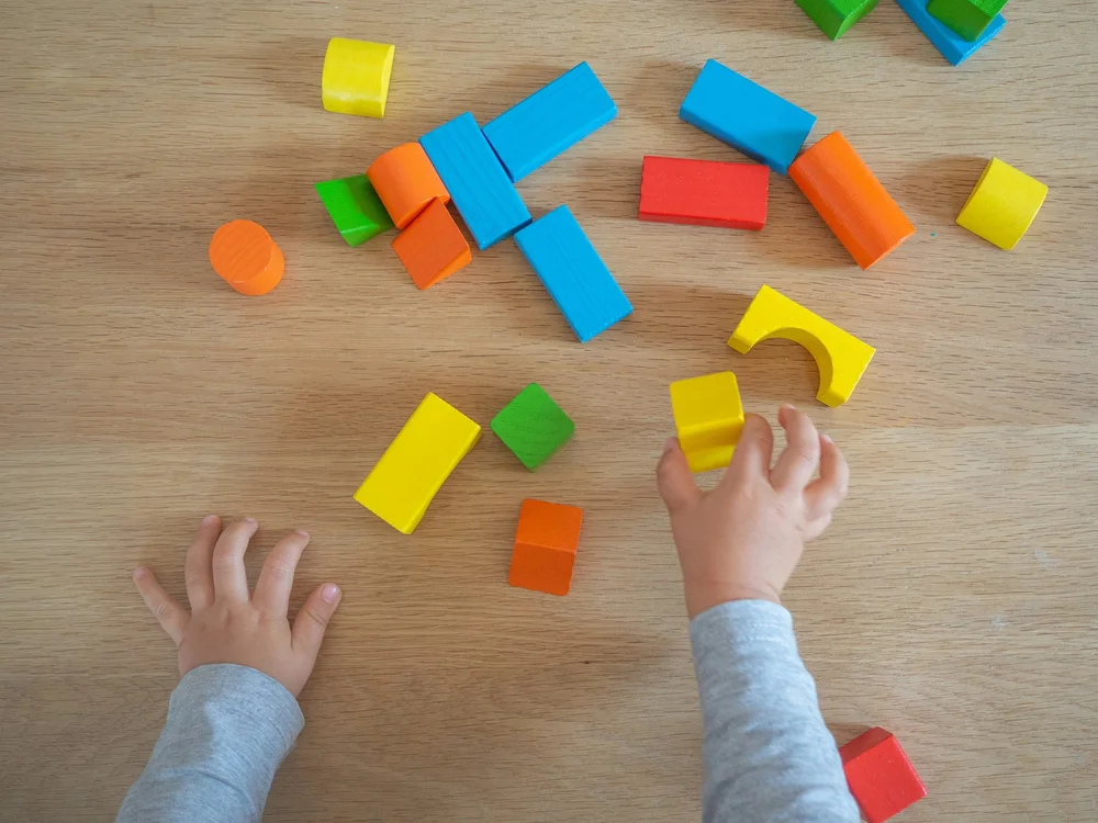 A child's hands sorting coloured wooden blocks on a wooden floor