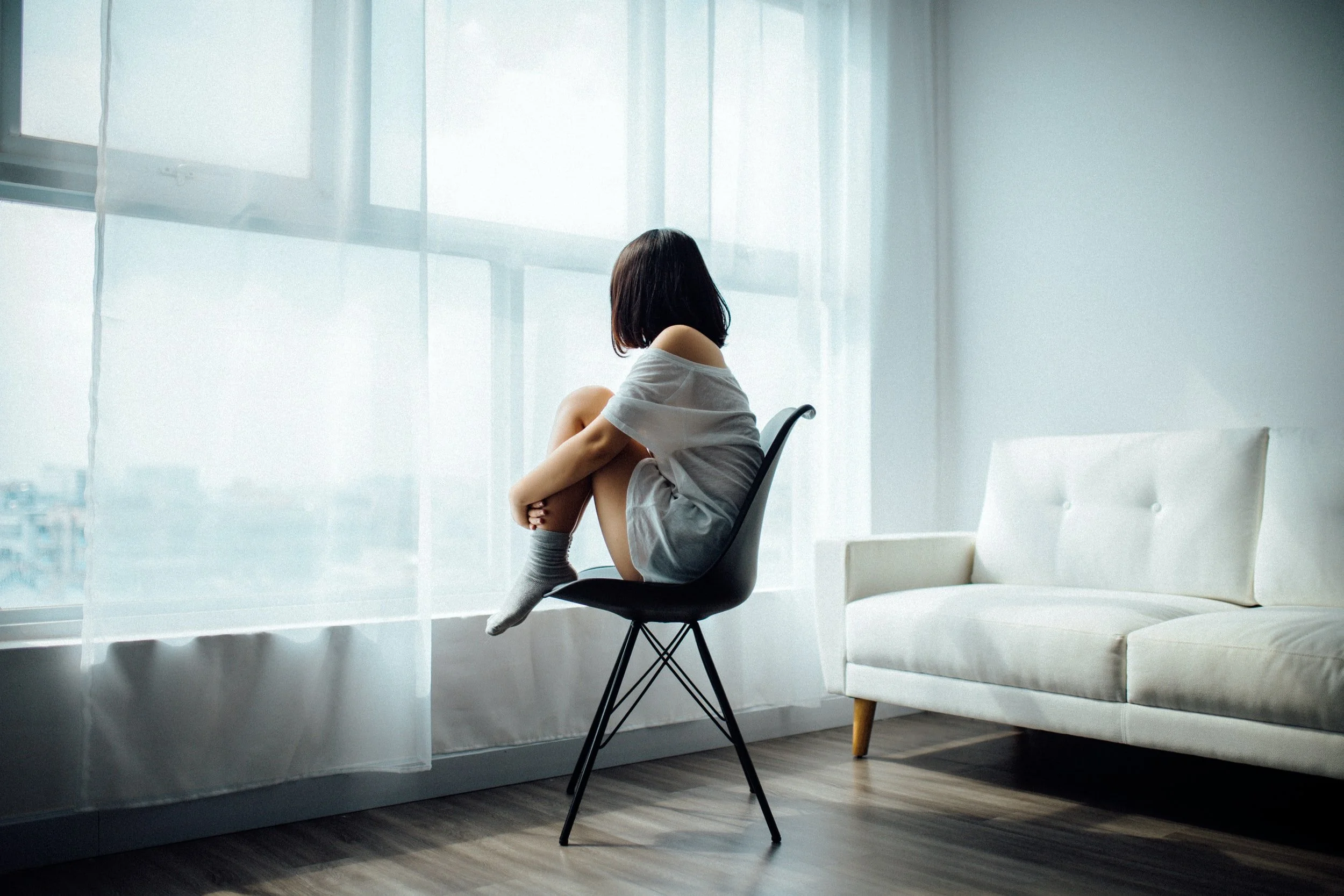 A child sitting alone on a chair, looking out a bright window