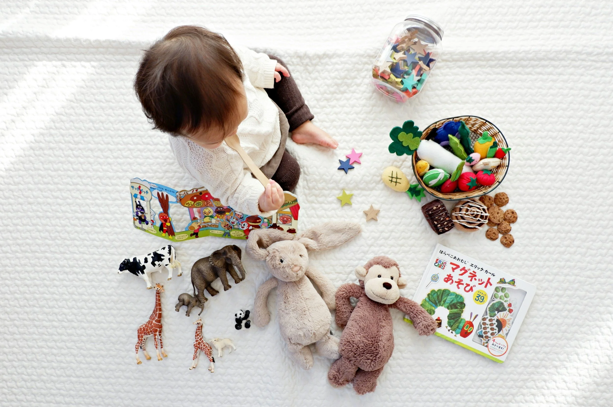 Overhead view of a toddler on a play mat surrounded by soft toys and books