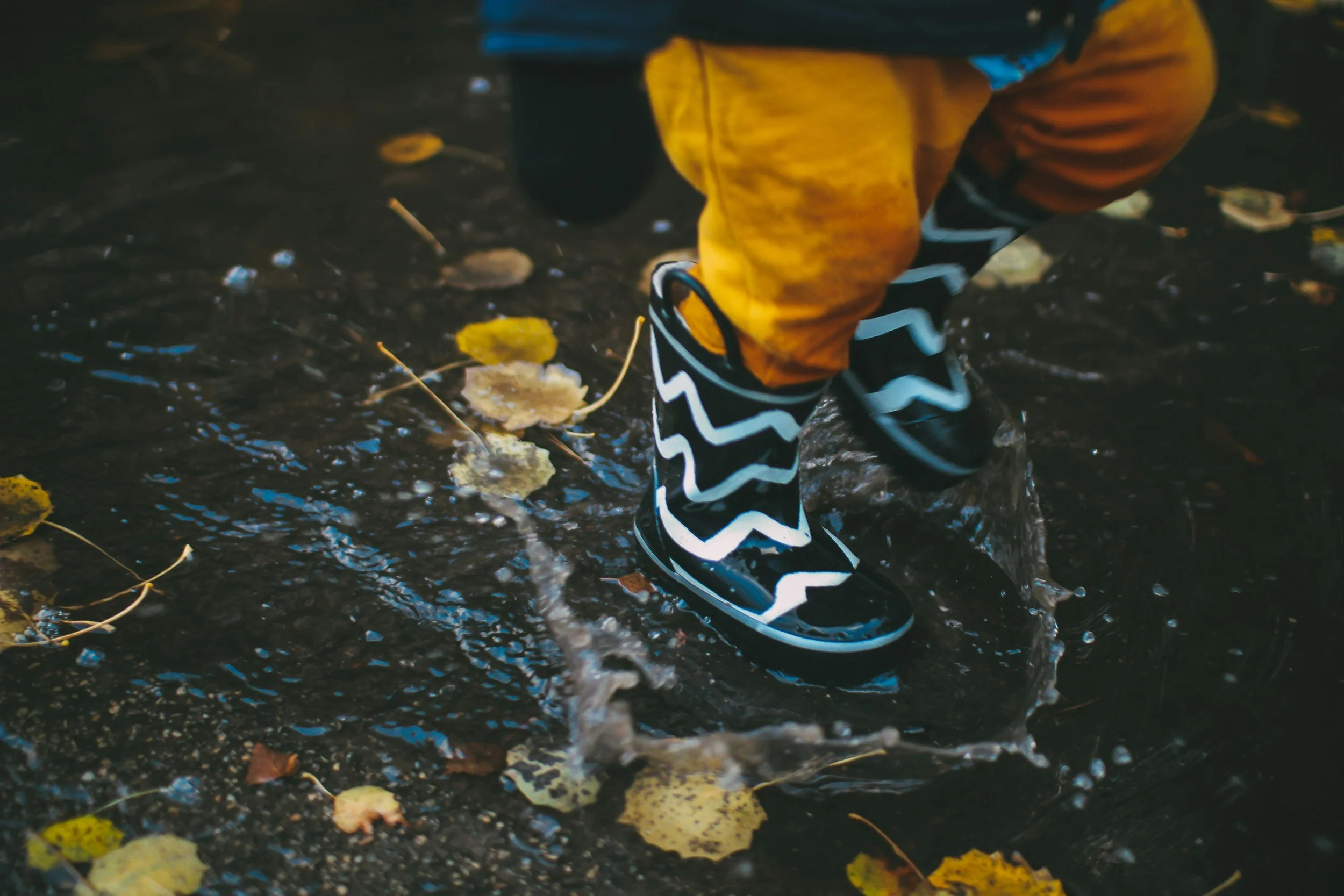 A child in rain boots jumping in a puddle