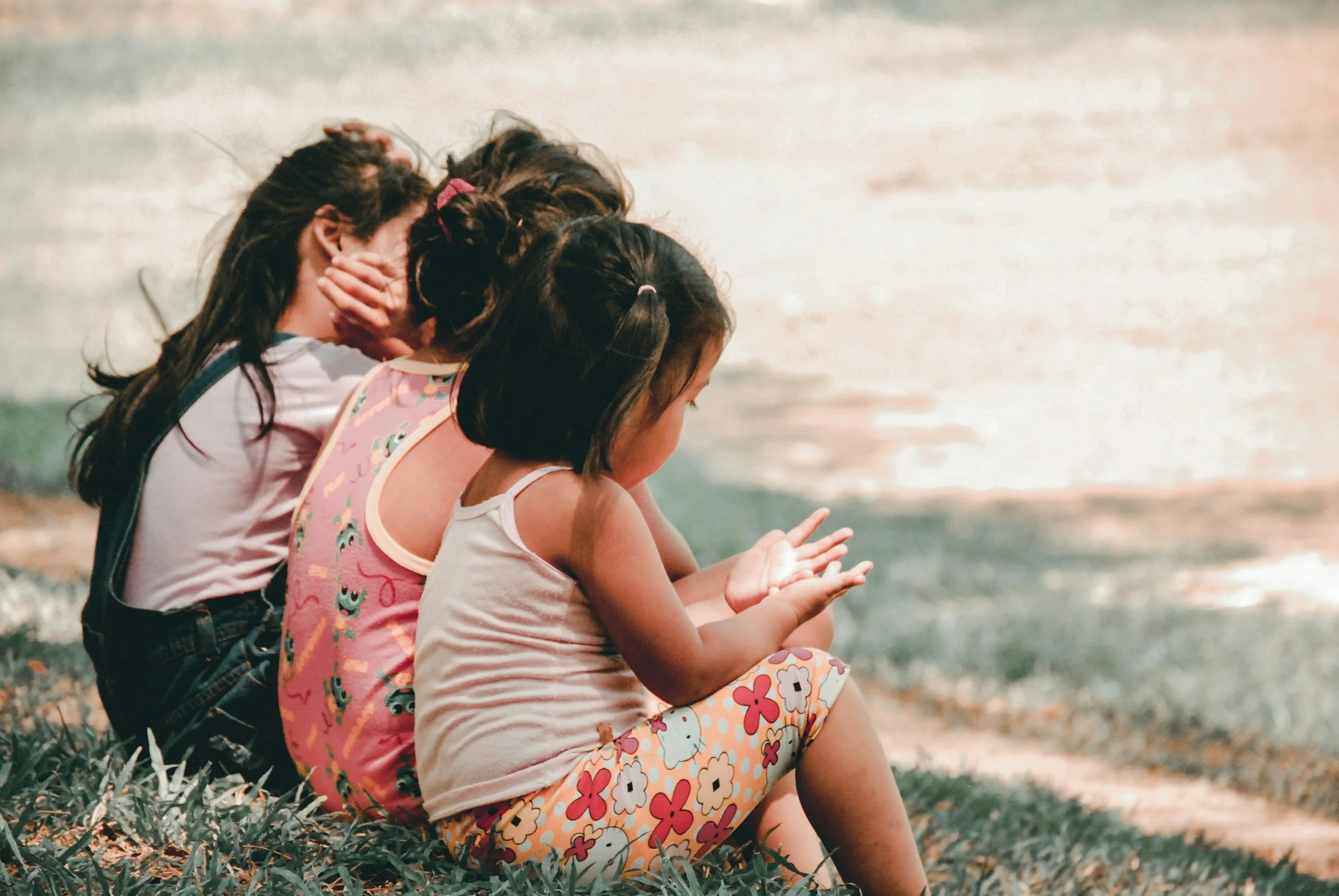 Three children sitting together on the grass with their arms around each other
