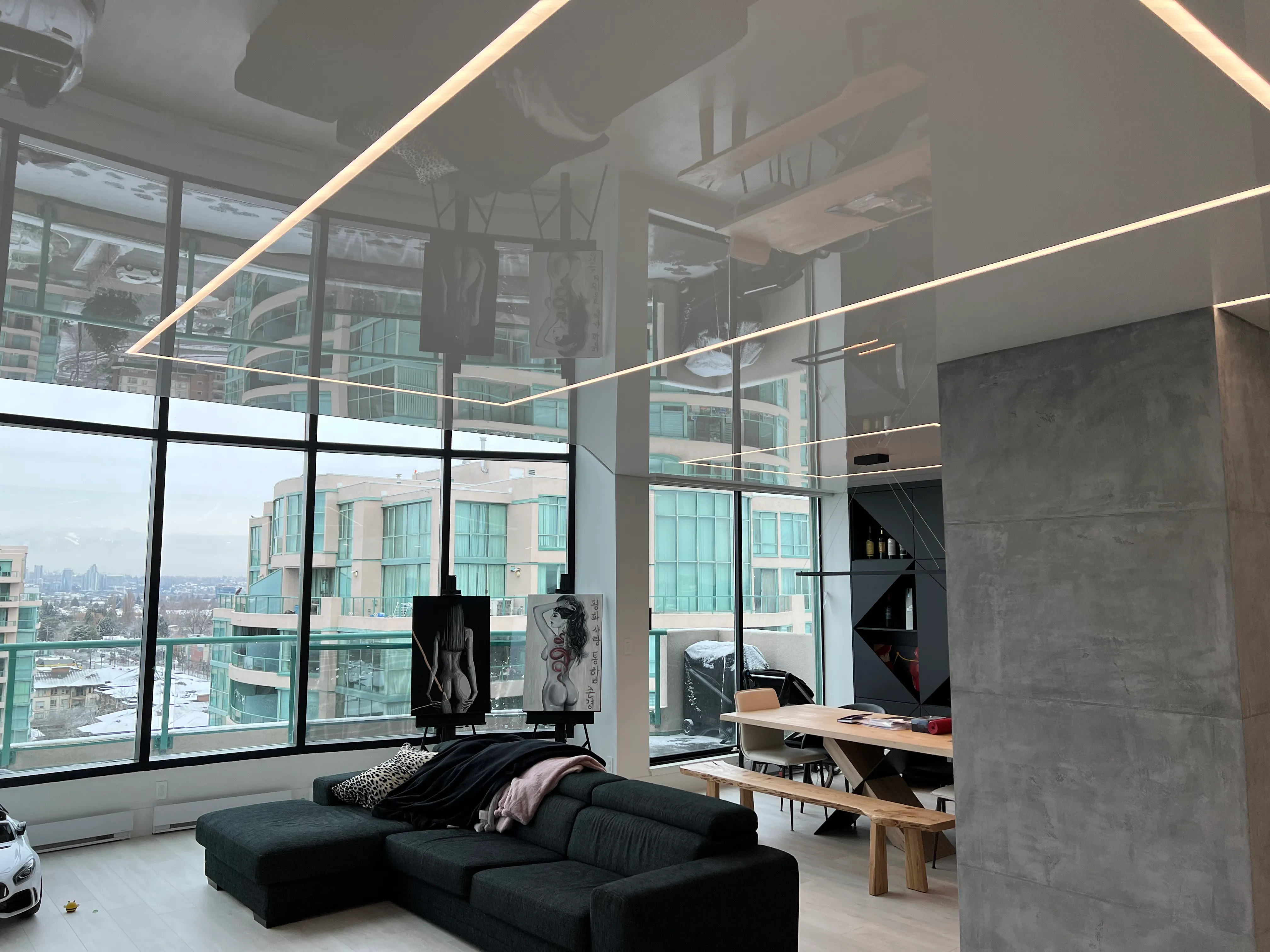 Double-height Vancouver living room with a gloss stretch ceiling reflecting the space and recessed linear LED runs