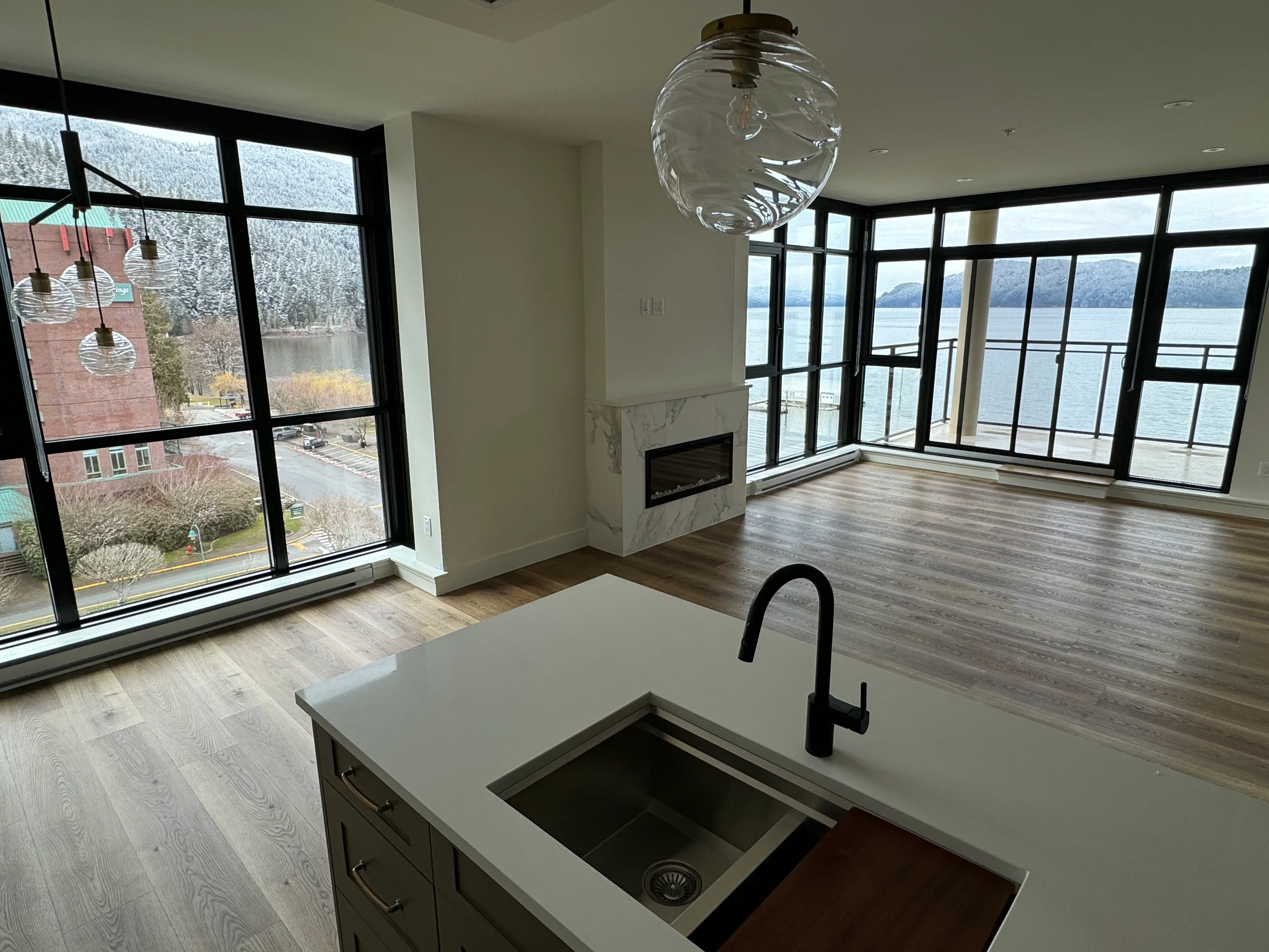 Waterfront living space with wide-plank hardwood flooring, a stone fireplace surround and full-height windows, finished by Luxury Interior in Metro Vancouver