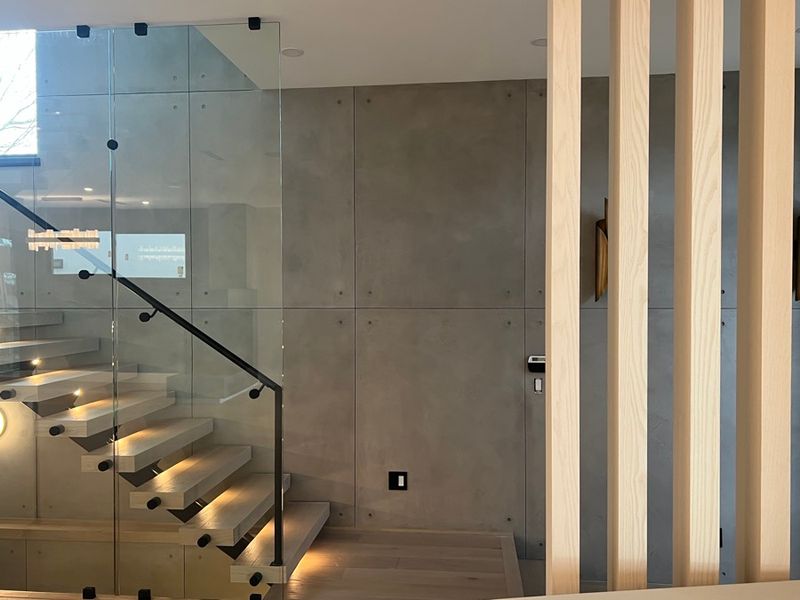 Floating stairs with lit treads beside a microcement wall and wood slats