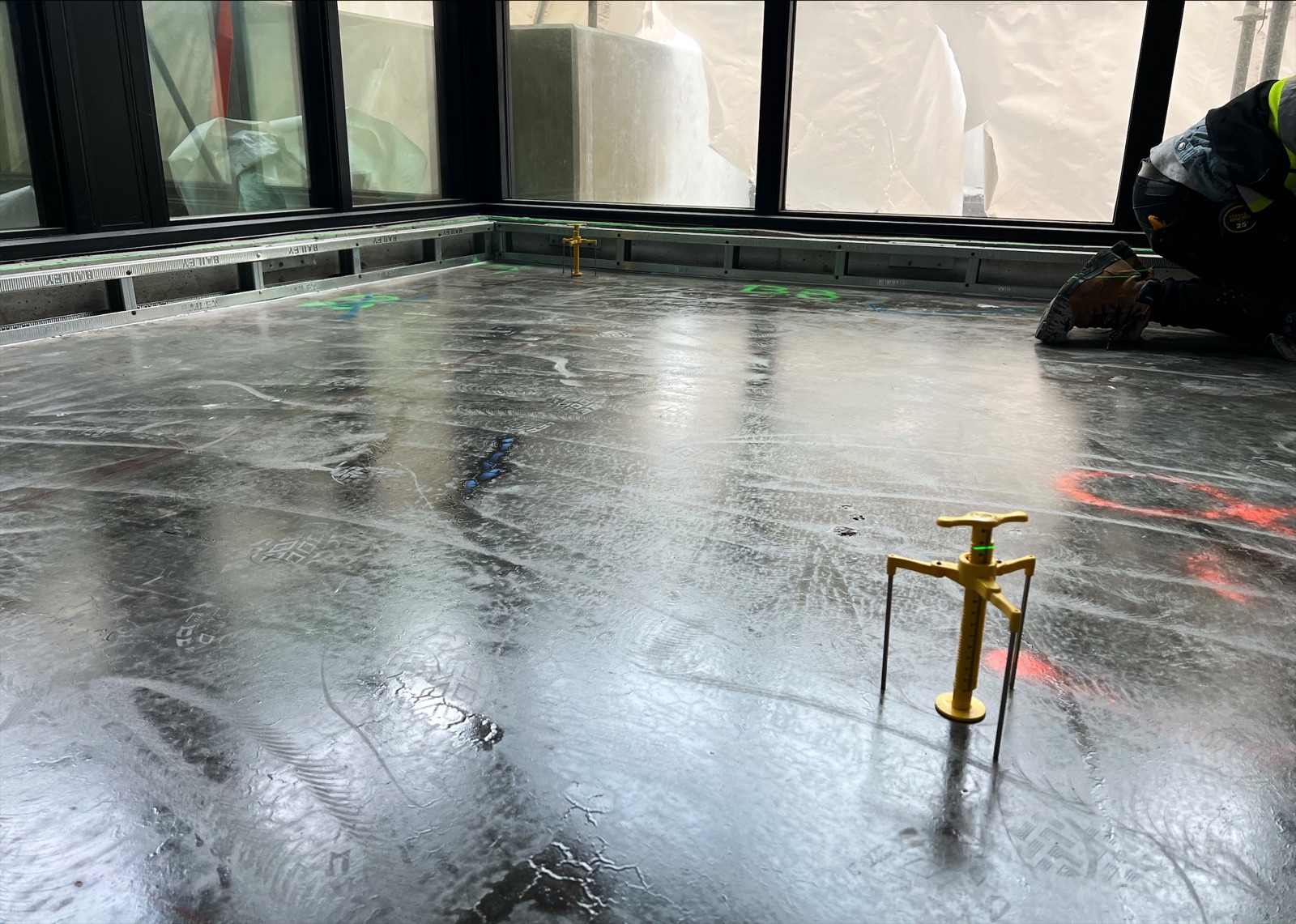 Worker kneeling at the edge of a wet levelling compound floor, yellow gauge in the foreground (Harrison Hot Springs)