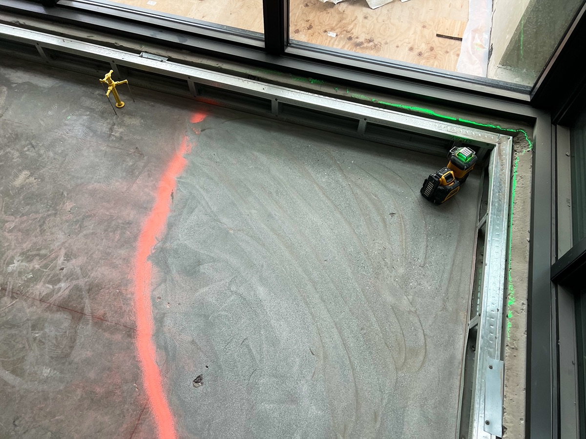 Laser level set up on the subfloor beside the window frame, orange marking line on the floor