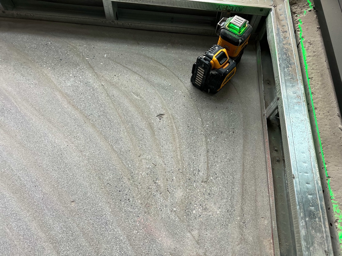 Yellow laser level in the corner of a room on a grey subfloor
