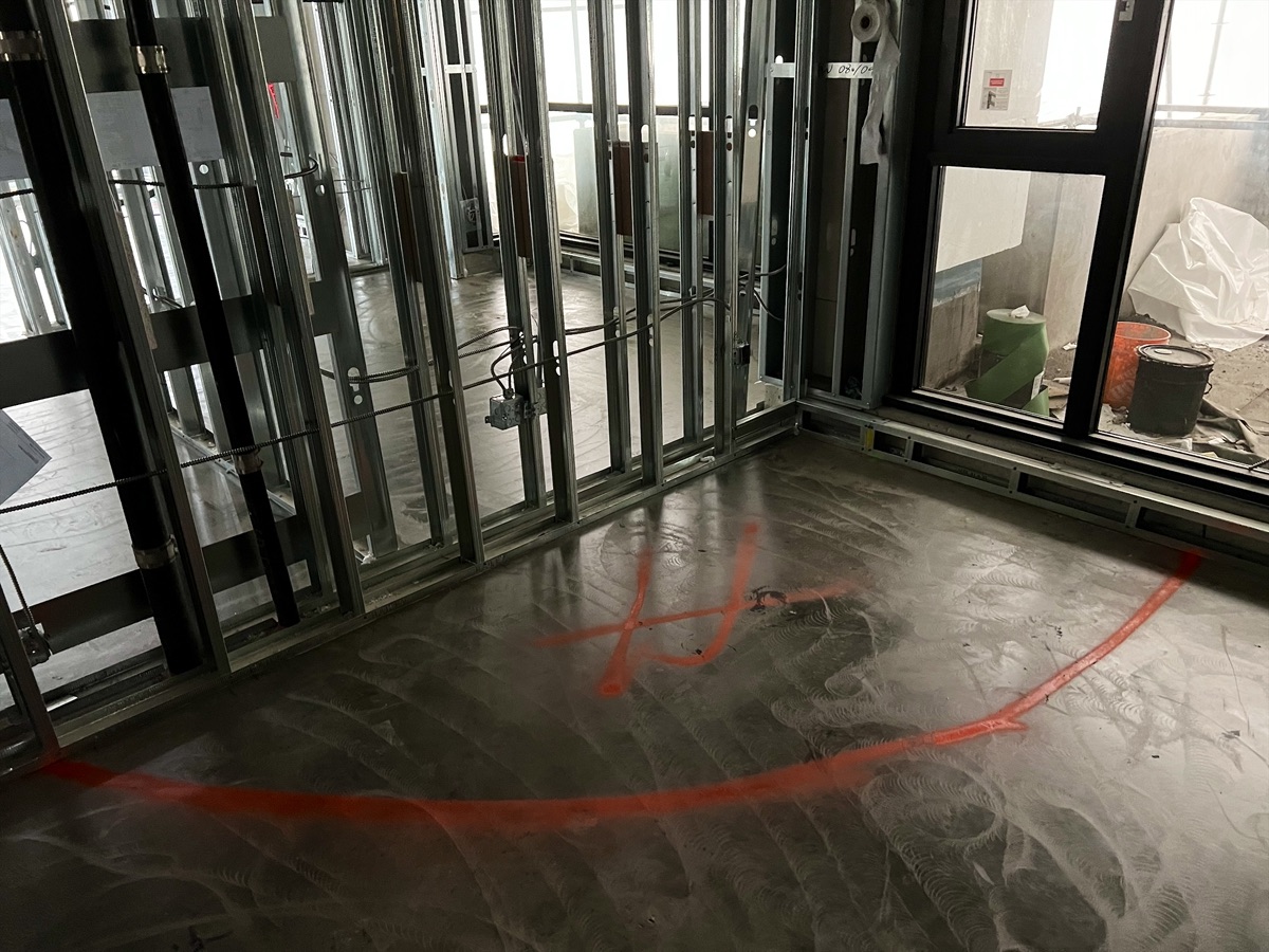 Subfloor with orange spray markings beside steel-stud partition walls and a window
