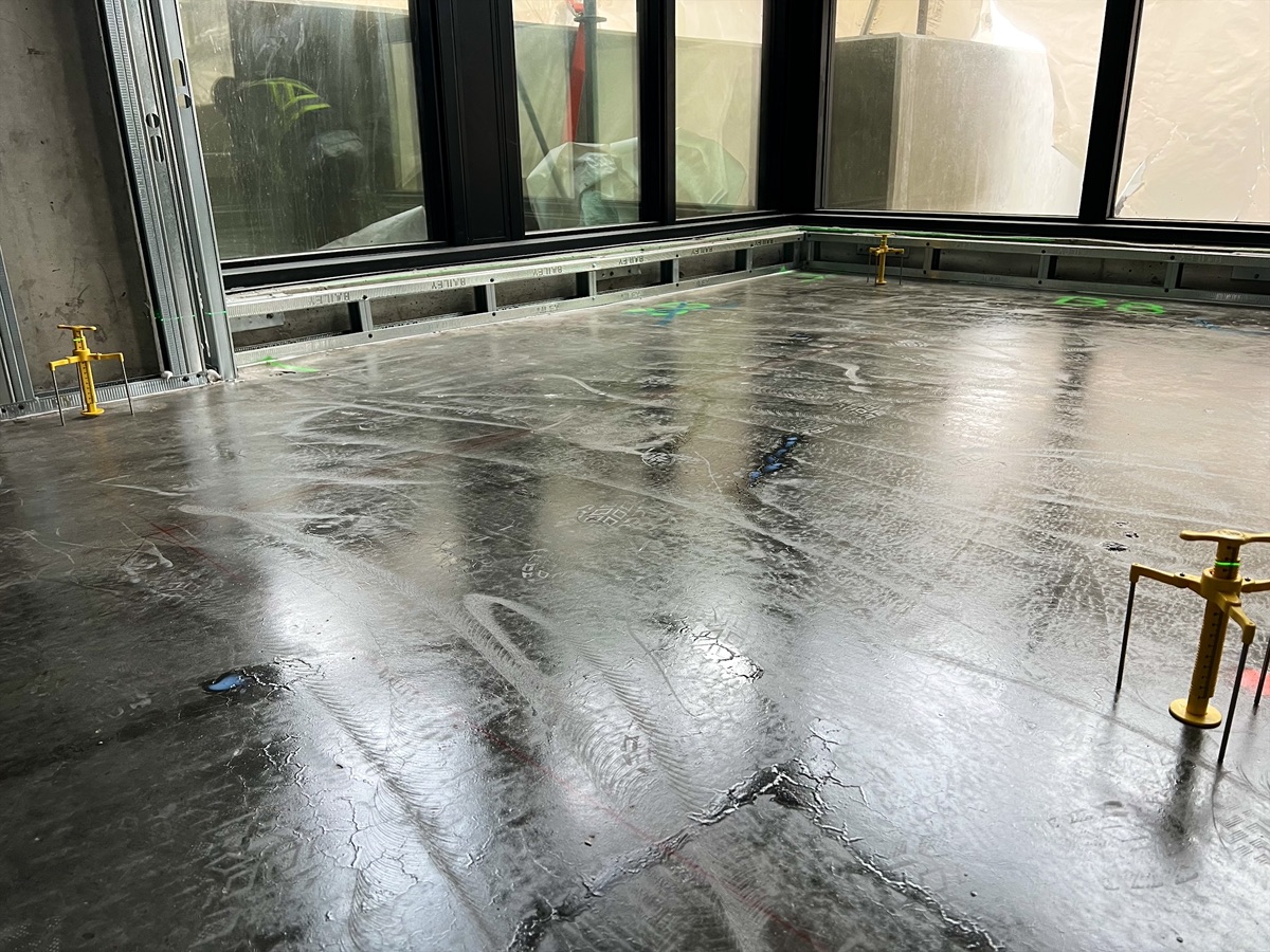Wet levelling compound across a corner room with windows, yellow gauges on the floor