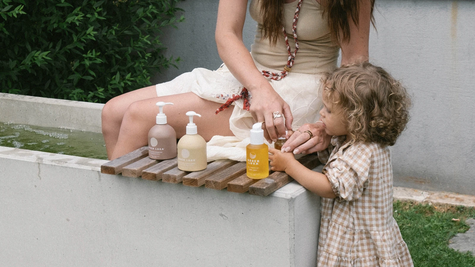 A mother and small child with Under Luna hair and body care bottles on a wooden ledge outdoors